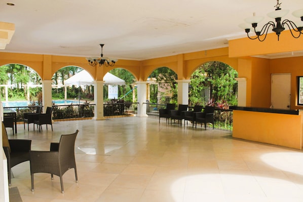 A spacious indoor area with a reception desk, multiple seating arrangements, and a view of the outdoors through large windows.
