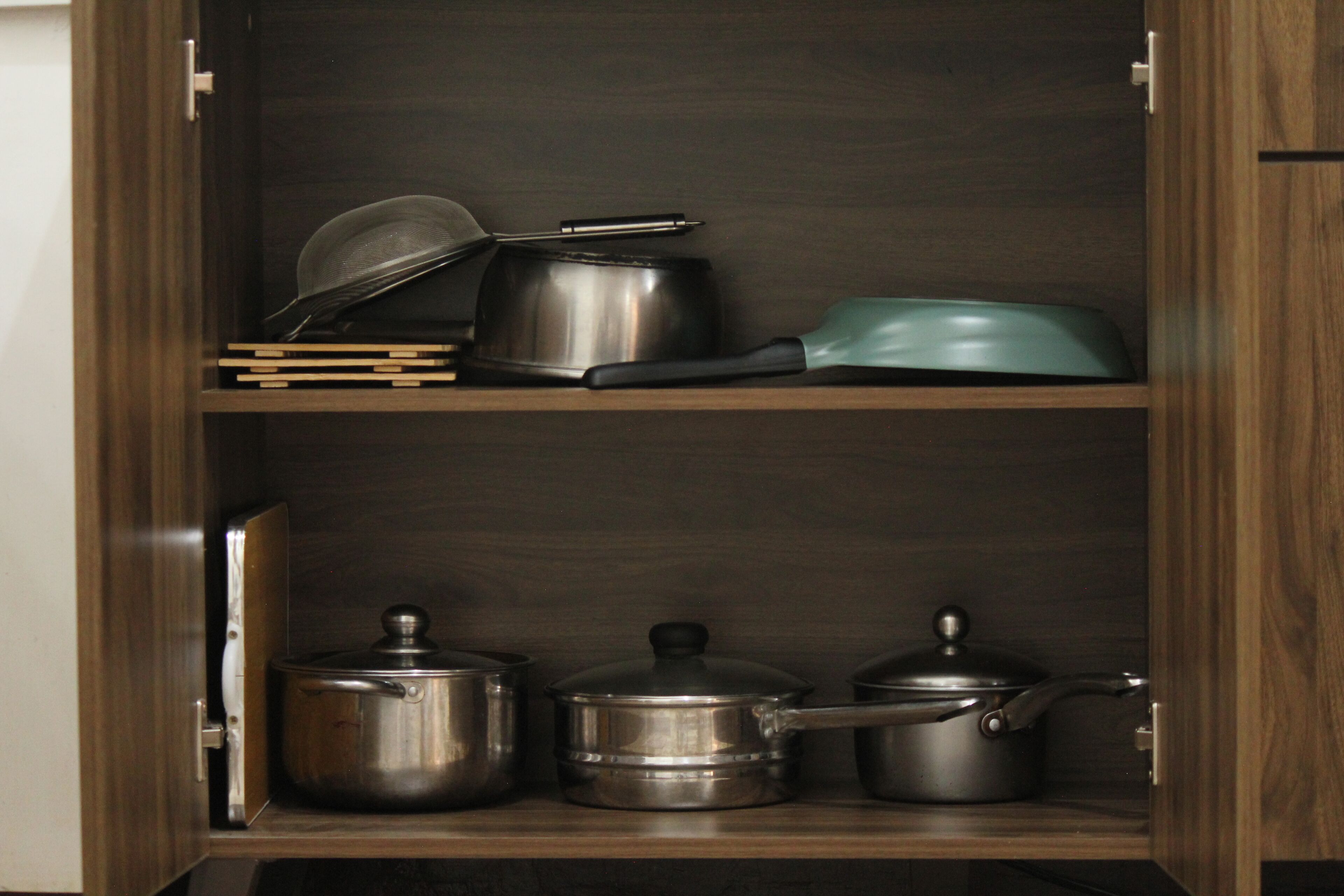 Um armário de cozinha com utensílios de aço inoxidável e uma panela verde.