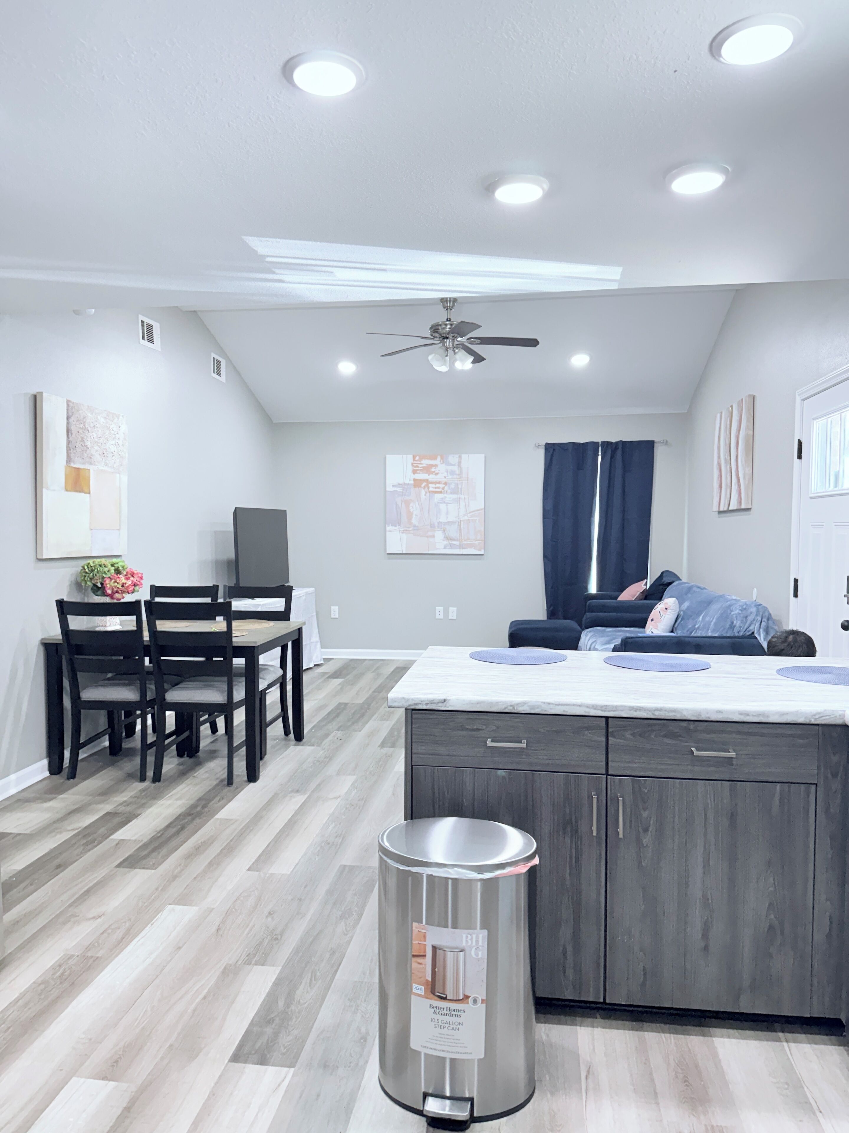 A modern kitchen with a central island, a dining area with chairs, and a ceiling fan.