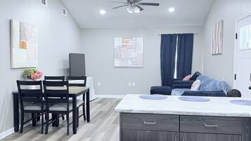 A modern kitchen with a central island, a dining area with chairs, and a ceiling fan.