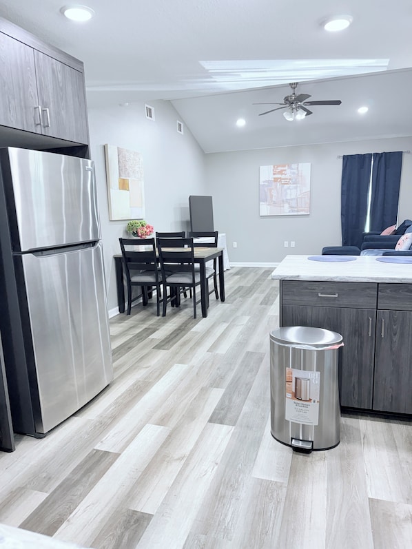 A modern kitchen with a built-in refrigerator, a dining area with a table and chairs, and a ceiling fan.