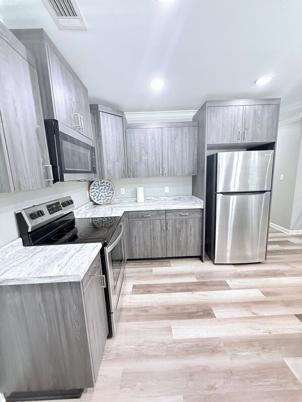 A modern kitchen with grey cabinetry, a stainless steel refrigerator, and a black stove.