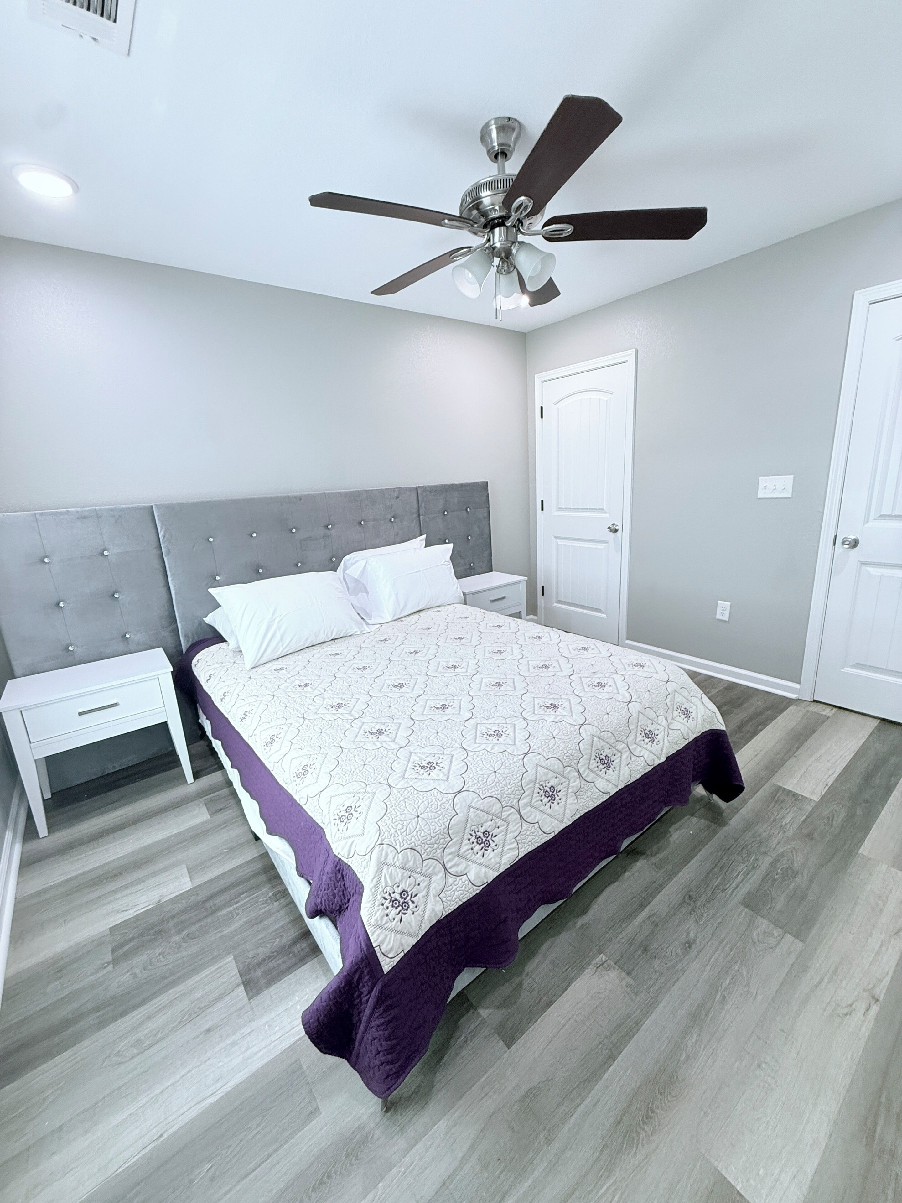 A bedroom with a bed, nightstands, a ceiling fan, and a door.