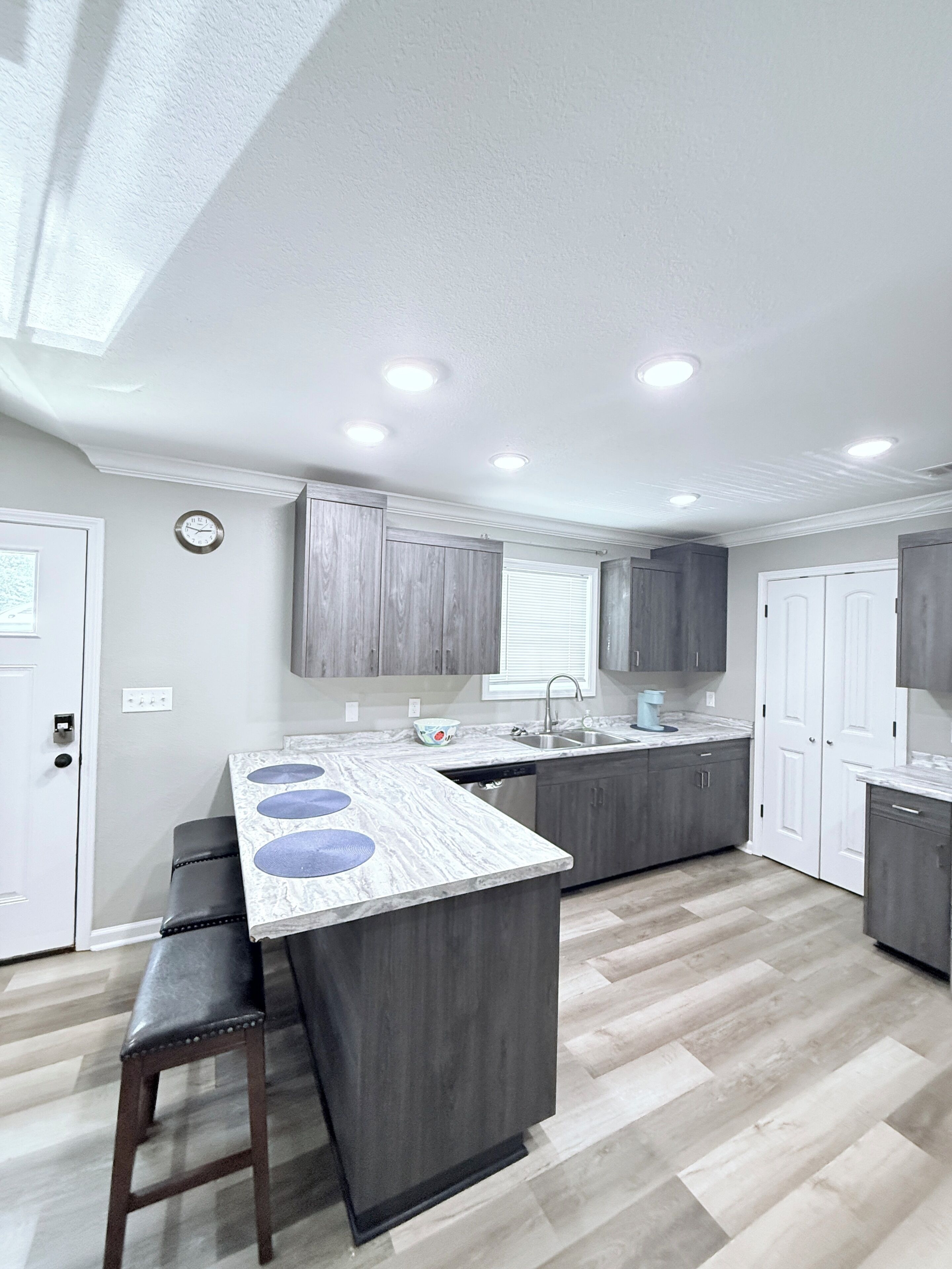 A modern kitchen with a central island, built-in cabinets, and a window with blinds.