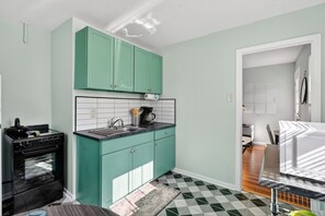 A compact kitchen with teal cabinets, a black stove, and a patterned rug. - Cute Clean 1br Close to the Quarter #3 (New Orleans)