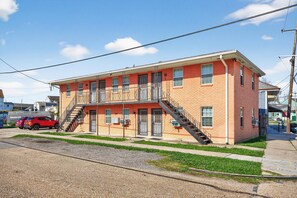 A two-story brick building with a flat roof, a central staircase, and a red car parked in front. - Cute Clean 1br Close to the Quarter #3 (New Orleans)