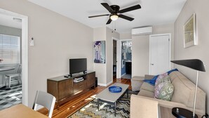 Un soggiorno moderno con una TV a schermo piatto, una ventola a soffitto, un divano e un'area pranzo con tavolo e sedie.
