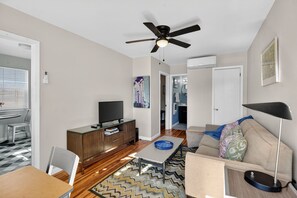 Ein modernes Wohnzimmer mit Flachbildfernseher, Deckenventilator, einer Couch und einem Essbereich mit Tisch und Stühlen.