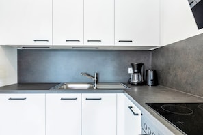 Una cocina moderna con armarios blancos, un lavamanos de acero inoxidable, una cafetera y una placa de inducción.