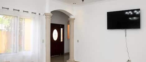 A living room with a sofa, a television mounted on the wall, and a door leading to another room.