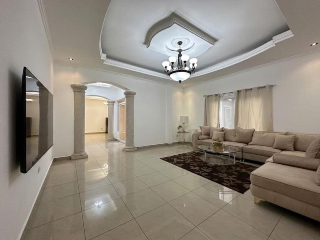 A spacious living room with a large sofa, a coffee table, and a chandelier.