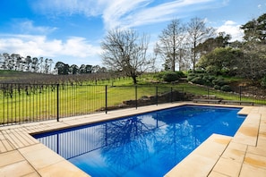 A swimming pool with a black metal fence, surrounded by a grassy area and trees. - Whispering Vines Scenic Country Retreat with Pool (Balhannah)