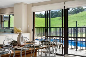 A dining area with a view of a swimming pool and a grassy landscape. - Whispering Vines Scenic Country Retreat with Pool (Balhannah)
