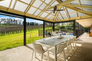 A covered outdoor area with a table and chairs, a pool, and a vineyard view. - Whispering Vines Scenic Country Retreat with Pool (Balhannah)