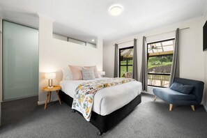 Ein Hotelzimmer mit einem Bett, einem Sessel, einem Nachttisch und einem Fenster mit Blick auf eine grüne Landschaft.