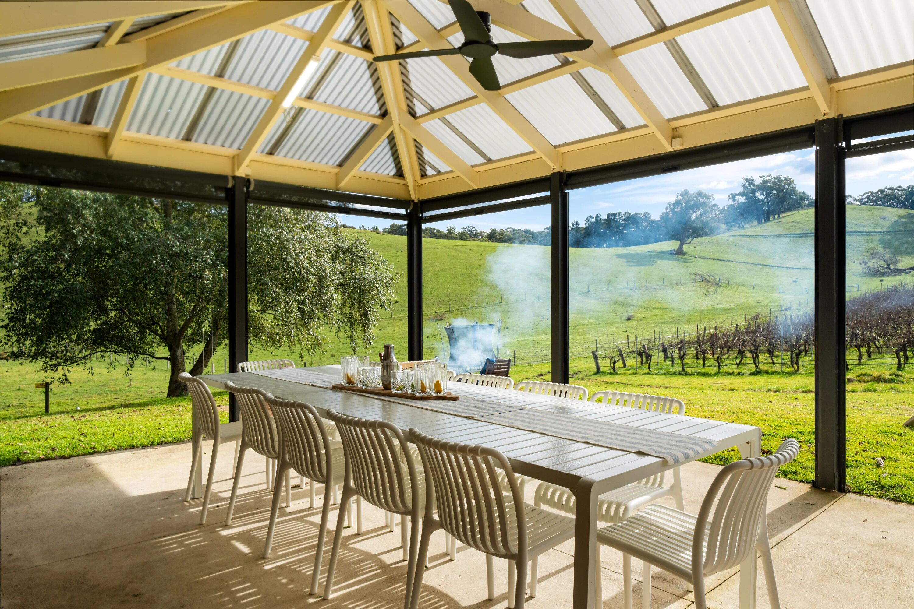 An outdoor patio with a table and chairs, a ceiling fan, and a view of a vineyard.