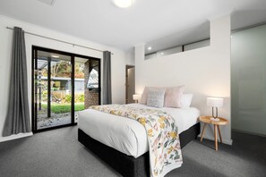 A bedroom with a bed, a bedside table, and a view of a garden through a sliding door. - Whispering Vines Scenic Country Retreat with Pool (Balhannah)