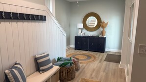 A modern interior with a bench, a round mirror, a dark-colored cabinet, and a ceiling fan. - Sweet SeaRenity- SURF CITY -New Luxury 4B, Ocean Views, Steps to Beach, Elevator (Surf City)