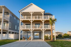 A multi-story residential building with a balcony on each floor, a covered entryway, and a palm tree in the foreground. - Sweet SeaRenity- SURF CITY -New Luxury 4B, Ocean Views, Steps to Beach, Elevator (Surf City)