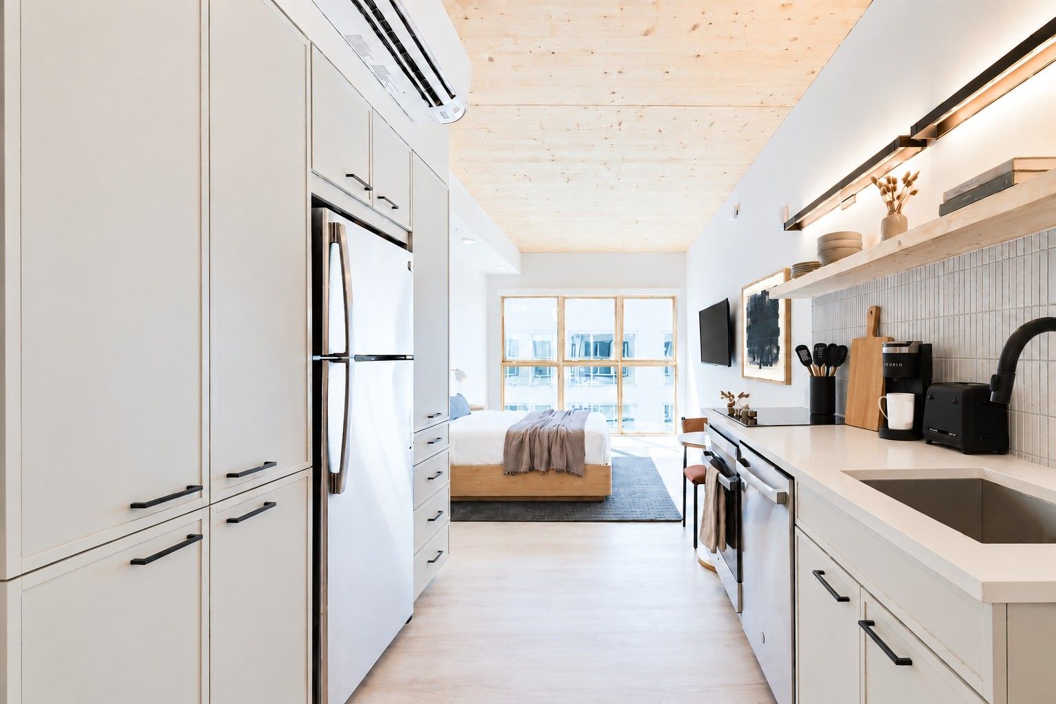 A modern kitchen with white cabinetry, a built-in oven, and a large window providing natural light.