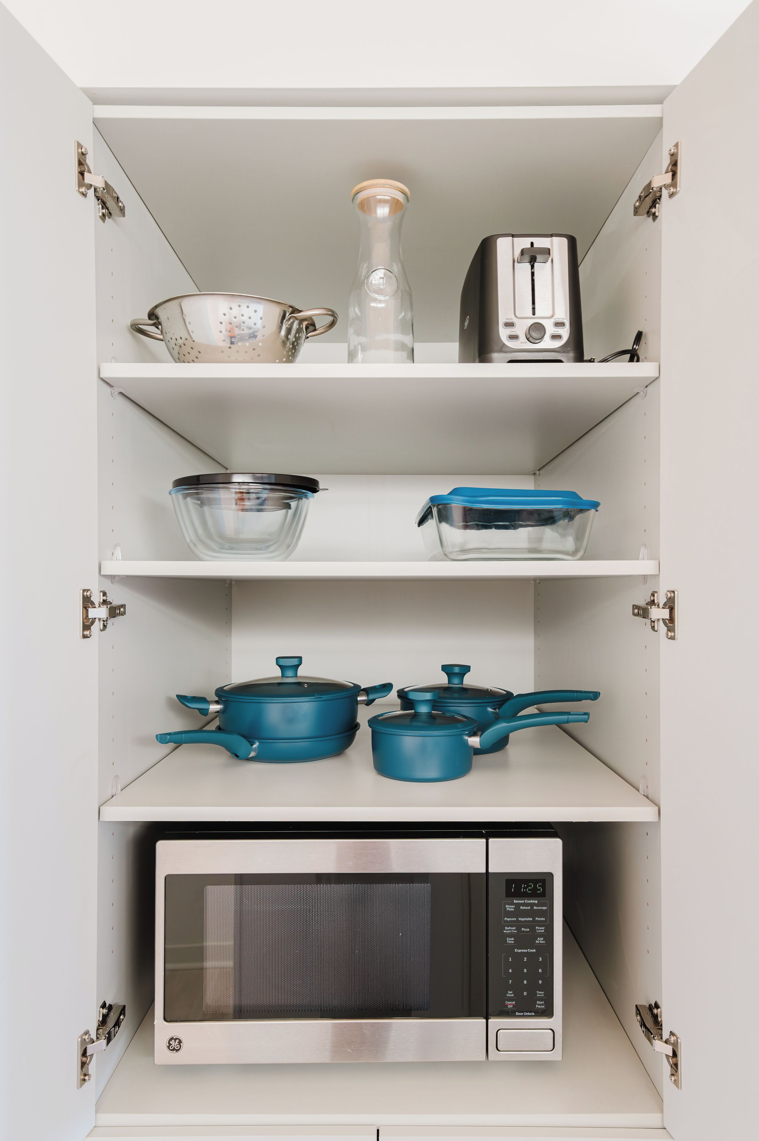 A kitchen with a microwave, pots, a colander, and a toaster on the shelves.