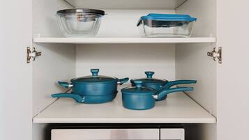 A kitchen with a microwave, pots, a colander, and a toaster on the shelves.
