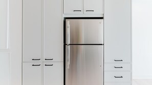 A stainless steel refrigerator in a kitchen with white cabinets and black handles.