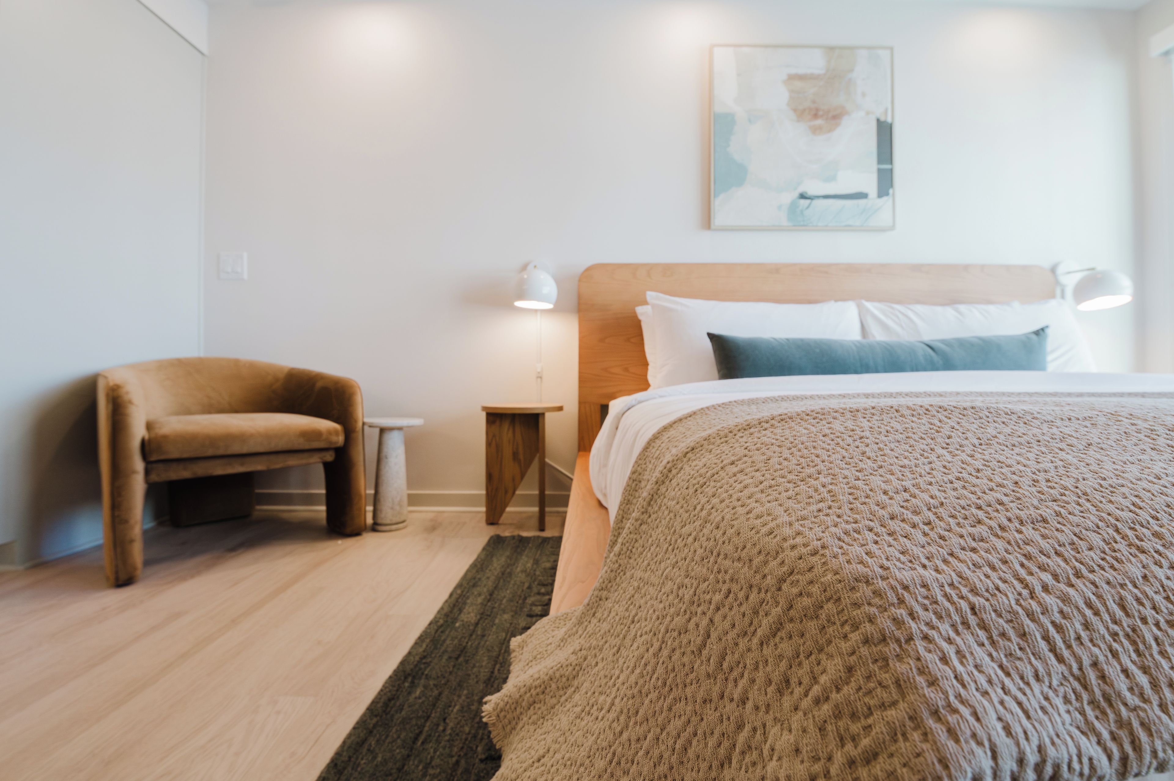 Une chambre d’hôtel avec un lit, une chaise, une petite table et une lampe fixée au mur.