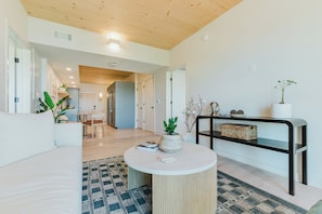 A modern living room with a round coffee table, a sofa, a dining area with a table and chairs, and a hallway leading to another room.