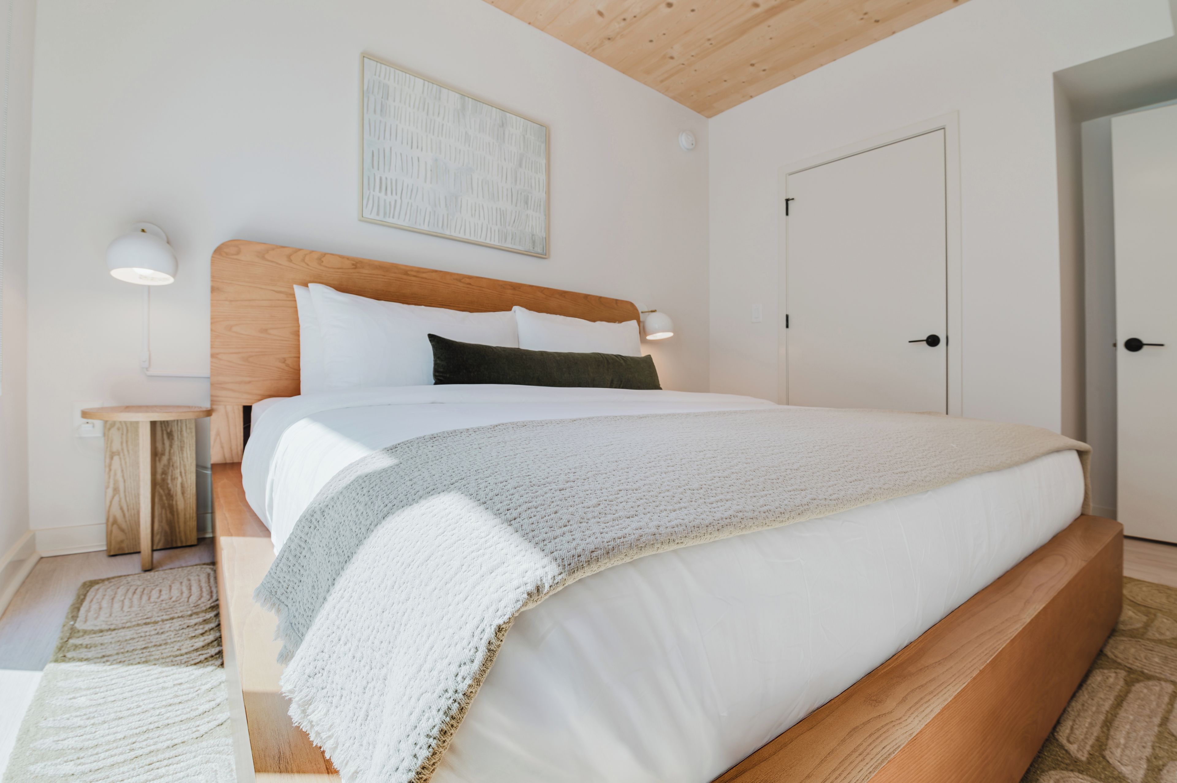 A bedroom with a large bed, a bedside table, a lamp, and a door.