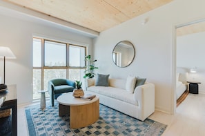 A modern living room with a sofa, a coffee table, a potted plant, and a large window. - Oxbow (Charlotte)