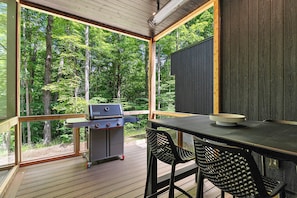 Eine Terrasse im Freien mit Grill, Tisch und Stühlen, umgeben von einem Wald.