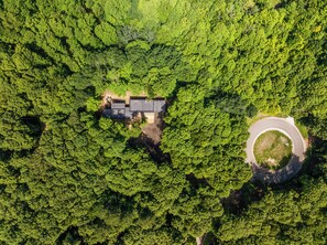 Vista aérea de uma propriedade com entrada circular, rodeada por floresta densa.