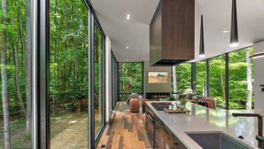 A modern kitchen with large windows, a central island, and a view of a forest. - The Linehouse at Norstead (Cedar)