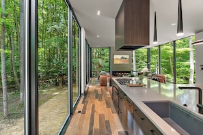 Eine moderne Küche mit großen Fenstern, einer zentralen Kochinsel und Blick auf einen Wald.