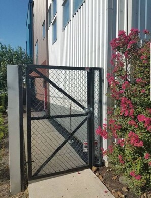 Ein begrenzter Zugang mit einem Metallgitter und einem Betonweg, der zu einem Gebäude mit vertikaler Verkleidung führt.