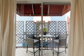 Ein Balkon mit Tisch, zwei Stühlen, einem Blumentopf und einem Metallzaun.