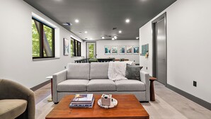 A modern living room with a grey sofa, a wooden coffee table, and a dining area in the background. - The Treehouse at Norstead (Cedar)