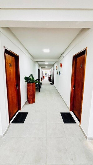 Un couloir d’hôtel avec deux portes en bois, une plante en pot et un sol carrelé.