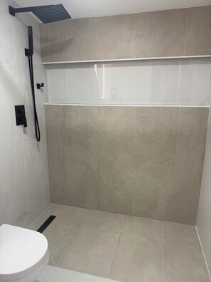 Ein Badezimmer mit Dusche, Toilette und gefliesten Wänden.