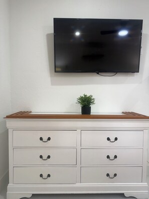 Eine weiße Kommode mit Schubladen und ein Flachbildfernseher, der darüber an der Wand befestigt ist.