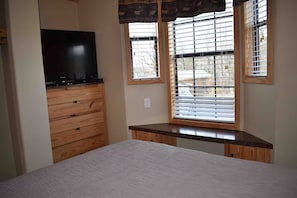 A bedroom with a bed, a wooden dresser, a television, and a window with blinds. - Acadian Shores Cabins - Lake View Cabin 4 (Zwolle)