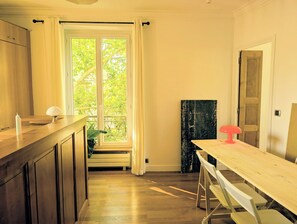 Eine Küche mit Holzschränken, einem Fenster mit Vorhängen, einem Esstisch mit Stühlen und einer Tür.