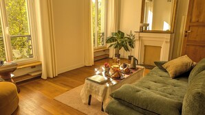 A cozy living room with a green sofa, a coffee table with breakfast items, a potted plant, and a fireplace. - Parisian charm, sunny apartment, beautiful views (Paris)