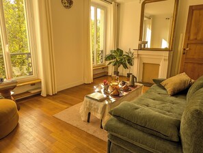 Ein gemütliches Wohnzimmer mit einem grünen Sofa, einem Couchtisch mit Frühstücksangeboten, einer Topfpflanze und einem Kamin.