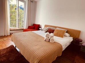 Ein Hotelzimmer mit einem großen Bett, einem Fenster mit Vorhängen und Blick auf Bäume.