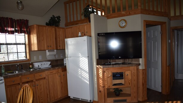 A compact kitchen with wooden cabinets, a white refrigerator, a built-in TV, and a small countertop.