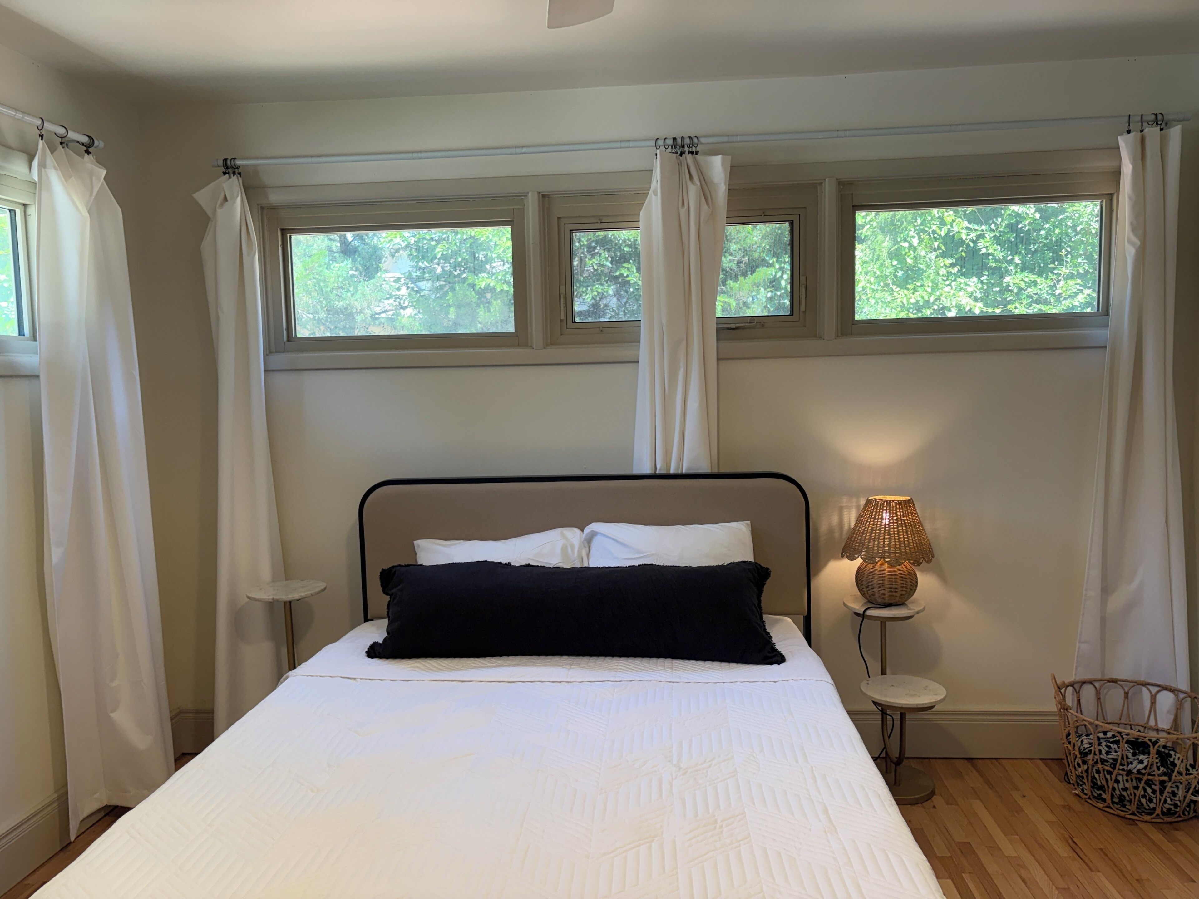 A bedroom with a bed, a bedside lamp, a small table, and a wicker basket.