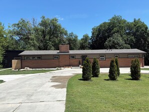 A two-story building with a brick facade and a flat roof, surrounded by a well-maintained lawn and several evergreen trees. - Spacious Ranch on Large Lot W Ample Parking (Wichita)