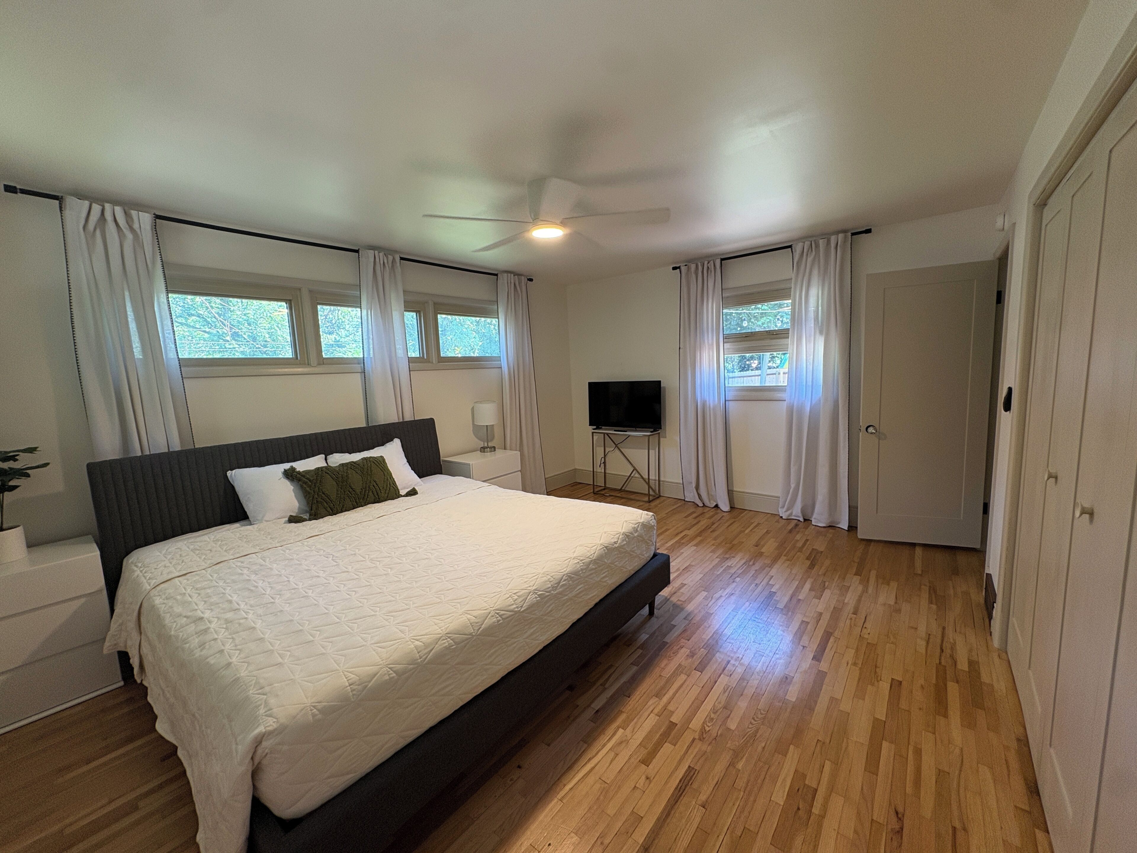 Un dormitorio con una cama grande, un televisor sobre un mueble y una puerta que da a otra habitación.